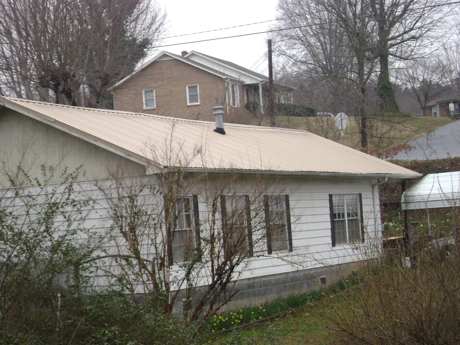 Tan metal roof on a white sided house set into a hillside — Commercial Roofing by Roofing Brothers in Cherry Valley